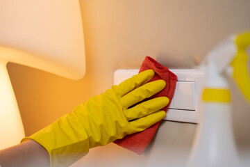 Hotel maid wipes white socket in hotel room using detergent. Woman in rubber gloves works in...