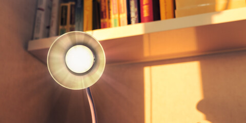 Electric modern lamp stands on desk against shelf with books at home at evening time. Studying and knowledge concept.