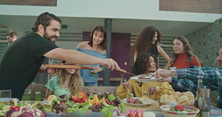 Barbecue chef serving food to friends and family at home backyard party. Happy people gathered together for lunch eating food