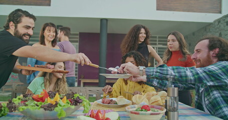 Barbecue chef bringing food and serving meat to friends and family united for party in backyard home garden BBQ. Happy people celebrating life