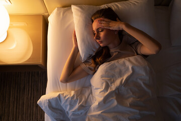Young woman tries to fall asleep tossing and turning in bed at night. Sleepless lady lies in hotel...