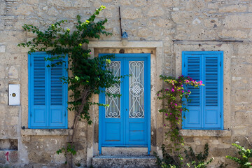 Fototapeta na wymiar View of old, historical, traditional stone house with blue colored door and windows in famous, touristic Aegean town called Alacati. It is a village of Cesme, Turkey. It is a sunny summer day