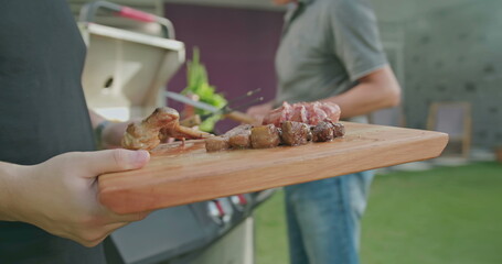 Barbecue chef serving food to friends and family at BBQ home backyard party. Happy people celebrating life with food