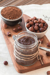 Homemade tasty cocoa cream with hazelnuts in a jar on a tableboard. Sweet and healthy food. Elevated view. Focus point.