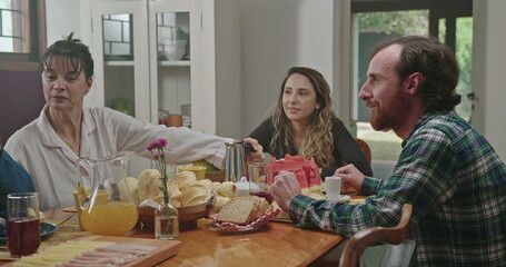 A happy family sitting together at table having breakfast in the kitchen. The daughter is drinking orange juice and chatting with her brother and parents.