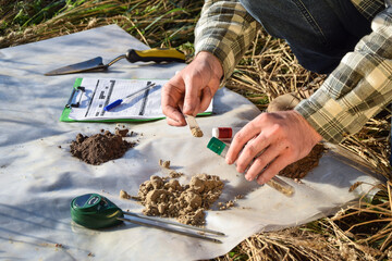 Closeup of male agronomy specialist taking soil sample in test tube outdoors, using laboratory...
