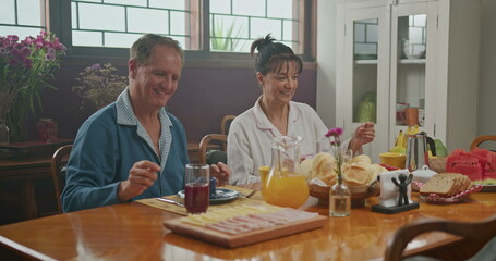 Married couple having breakfast together. The wife serves coffee to her husband. the two chat happily and enjoy a good cup of coffee wearing pajamas