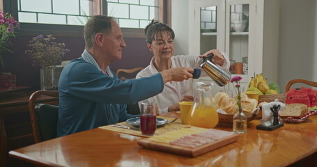 Married couple having breakfast together. The wife serves coffee to her husband. the two chat happily and enjoy a good cup of coffee wearing pajamas