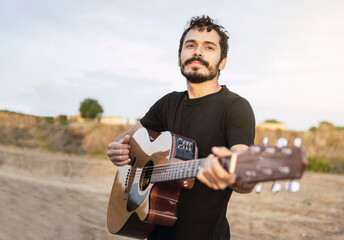 Portrait of young musician playing guitar on the road at sunset.
