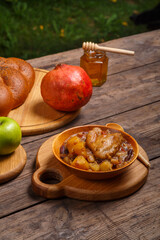 Chelnt with chicken in a wooden plate with a wooden spoon on the festive table for Rosh Hashanah next to apples, challah and pomegranate.
