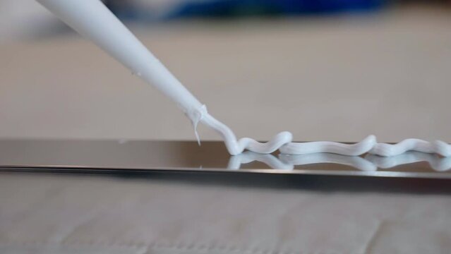 Close up shot of white glue applying in zig zag on metal profile surface, process of bonding material surfaces between them with industrial instruments. Adhesive glue or sealant for fixing, repairing