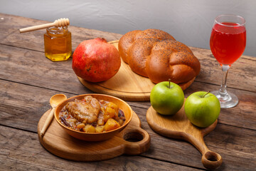 Chelnt with chicken in a wooden plate on the festive table for Rosh Hashanah next to challah honey and apples.