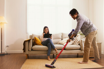 Wife happy that the husband does housework uses the living room carpet vacuum cleaner instead own duties sits on the sofa playing laptop interested in social networks, does not want to do housework.