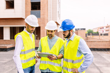 Group of professional engineer architects discussing plan on digital tablet at apartment building construction site