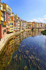 Houses of colorful colors on the banks of the river and reflection in the calm water on a sunny day, Girona, Catalonia.