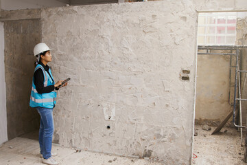 Obraz na płótnie Canvas Asian female architects design concrete walls on the construction site use laptop check the surface and want to use ceramic or raw concrete is in the process making decision for customers choose.