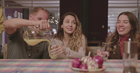 The family gathers around the table in the backyard in the evening to talk. The father serves juice to his daughters.