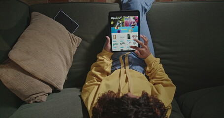 Woman holds tablet surfs online shopping sites. Girl sitting on couch browsing online retail store searching for product to buy