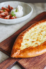 Traditional Turkish baked pide dish. Middle Eastern snacks. Turkish pizza. Turkish pide with cheese - Kasarli Pide and tomatoes with burrata cheese on grey concrete background. Selective focus