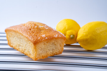 Home made Lemon Drizzle loaf tin cake on a stainless steel rack with lemons