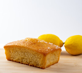 Lemon drizzle cake  and fresh lemons on a bamboo board with white background