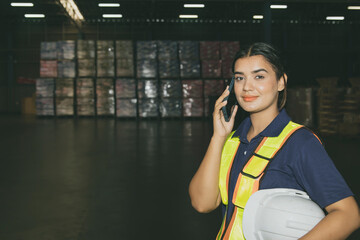 Warehouse worker, Portrait beautiful Indian woman holding smartphone confidently talking to work while looking at the camera : International export warehousing business concept.