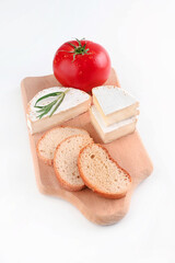baguette, camembert with rosemary and tomato on a wooden board on a white table.