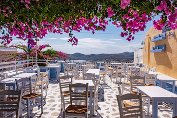 Empty Greek terrace restaurant with beautiful pink bougainvilleas and amazing view. Holiday destination Cyclades islands in Aegean sea, ​​Greece. Summer vacation background with copy space.