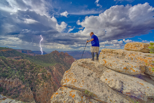A hiker standing on the summit of Buggeln Hill at Grand Canyon Arizona with a lightning storm in the distance.