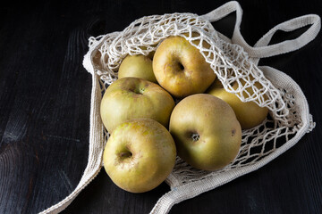 Aerial view of organic white mesh bag with pippin apples, on dark wooden table, horizontal