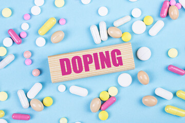 On a blue background, multi-colored pills and a wooden block with the text DOPING. View from above. Medical concept