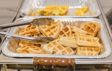 Golden brown waffles in an aluminum foil tray being served at a breakfast buffet or brunch.