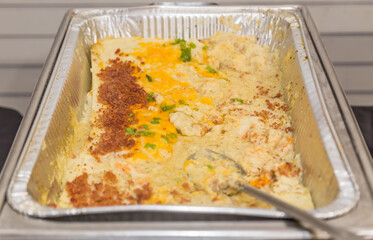 Loaded cheese grits in an aluminum foil pan being served a a brunch buffet.
