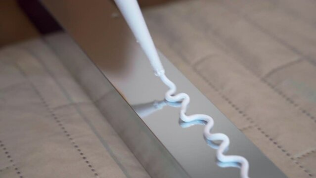 Top view shot of white glue applying on metal profile surface, workman applying sealant in zig zag for further installing. Repairing adhesive glue for fixing different types of surface, industrial