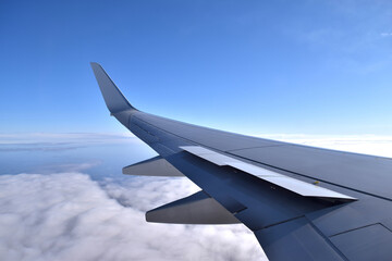 View from a plane window above clouds, with flaps up, before landing. Traveling on a clear sky day