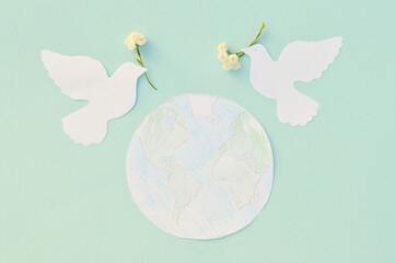 Two white pigeons, cut out of paper with live white flowers in their beaks, hover over a model of the planet Earth. The concept of the International Day of Peace