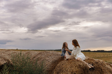 Mom and daughter are sitting on haystacks