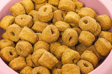 Dry food for cats or dogs macro photo. Animal feed in a pink bowl.
