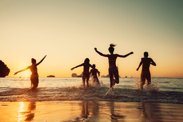 Happy young friends runs to sunset sea beach. Tropical vacations concept