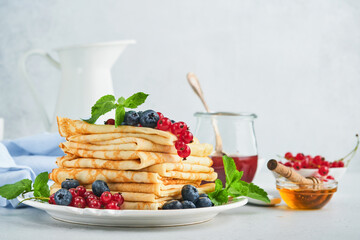 Pancakes. Stack of crepes or thin pancakes with berries, blueberries, red currants, raspberries and honey for breakfast. Homemade breakfast. Copy space. Selective focus.