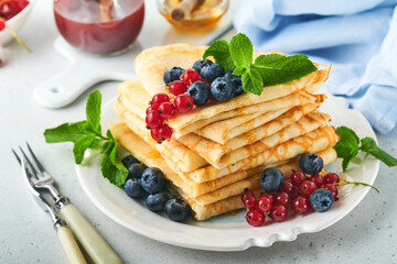 Pancakes. Stack of crepes or thin pancakes with berries, blueberries, red currants, raspberries and honey for breakfast. Homemade breakfast. Copy space. Selective focus.