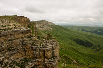 Naklejka premium Panoramic view of the canyon with green hills blurred by misty haze to the horizon and steep high cliffs of the Bermamyt plateau in Karachay-Cherkessia