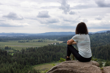 Naklejka na ściany i meble Adventurous Woman Standing on top of a rock overlooking the Canadian Nature Landscape. Minnekhada Regional Park, Coquitlam, Vancouver, British Columbia, Canada.