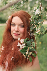 Naklejka premium redhead young woman with green eyes and freckles in white apple blossom