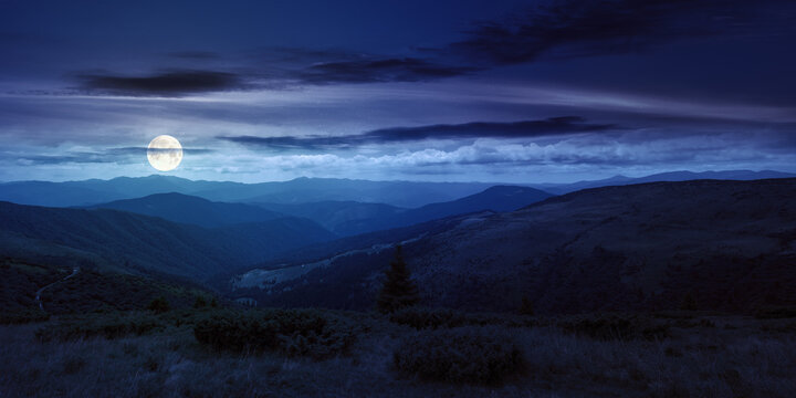 rolling hills and grassy meadows of carpathians. chornohora mountain ridge in the distance on a summer night with clouds on the sky in full moon light