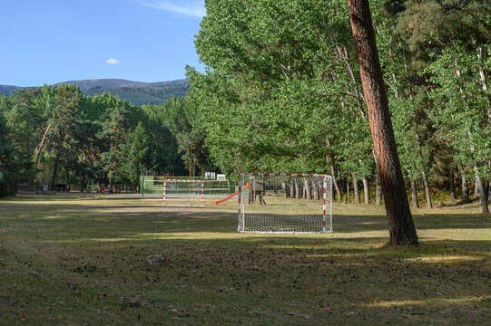 View of a football field, soccer, in the field, in the middle of a forest, right in the forest clearing enters the game field. Empty goals painted with red and white stripes and white netting. A big p
