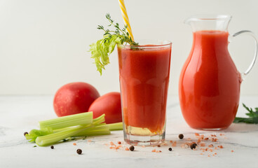 Fresh tomato juice in a glass with a straw on the white background. Red tomato juice cocktail with tomatoes and celery