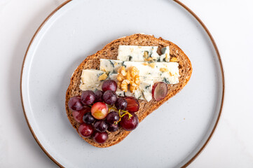Toasted bread with mild creamy blue cheese, grapes and walnuts on grey plate