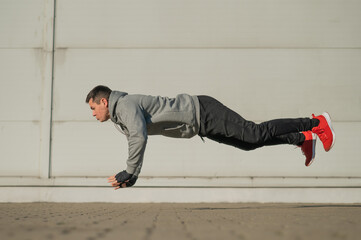 A man in a hoodie jumps while doing push-ups outdoors.
