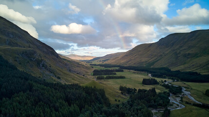 An aerial view of Glen Doll - mountains, pine forest and a river. Little rainbow in an evening sky.